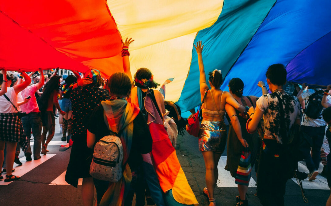 Un gruppo di persone marcia sotto la bandiera arcobaleno della pace.